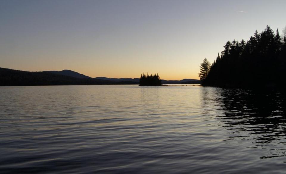 The sun rises behind silhouettes of trees and mountains over Cedar River Flow.